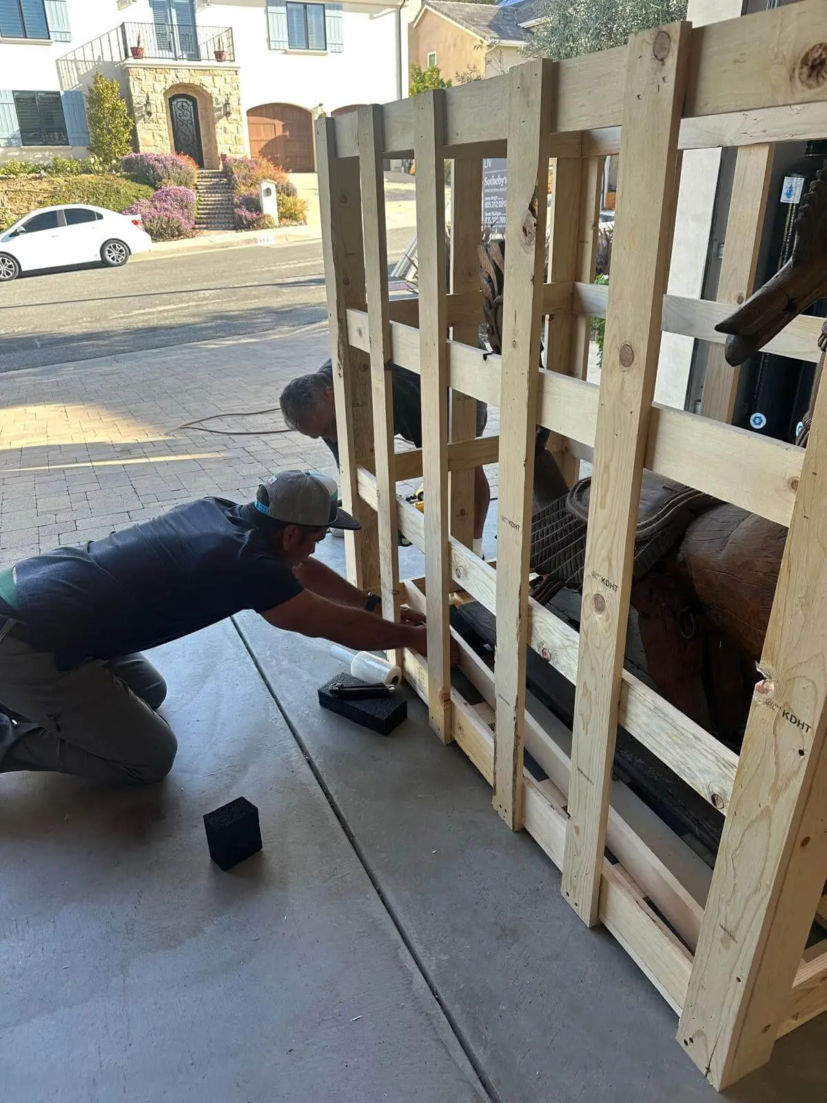 Two crew members assembling a slatted timber crate around a large sculpture on site.