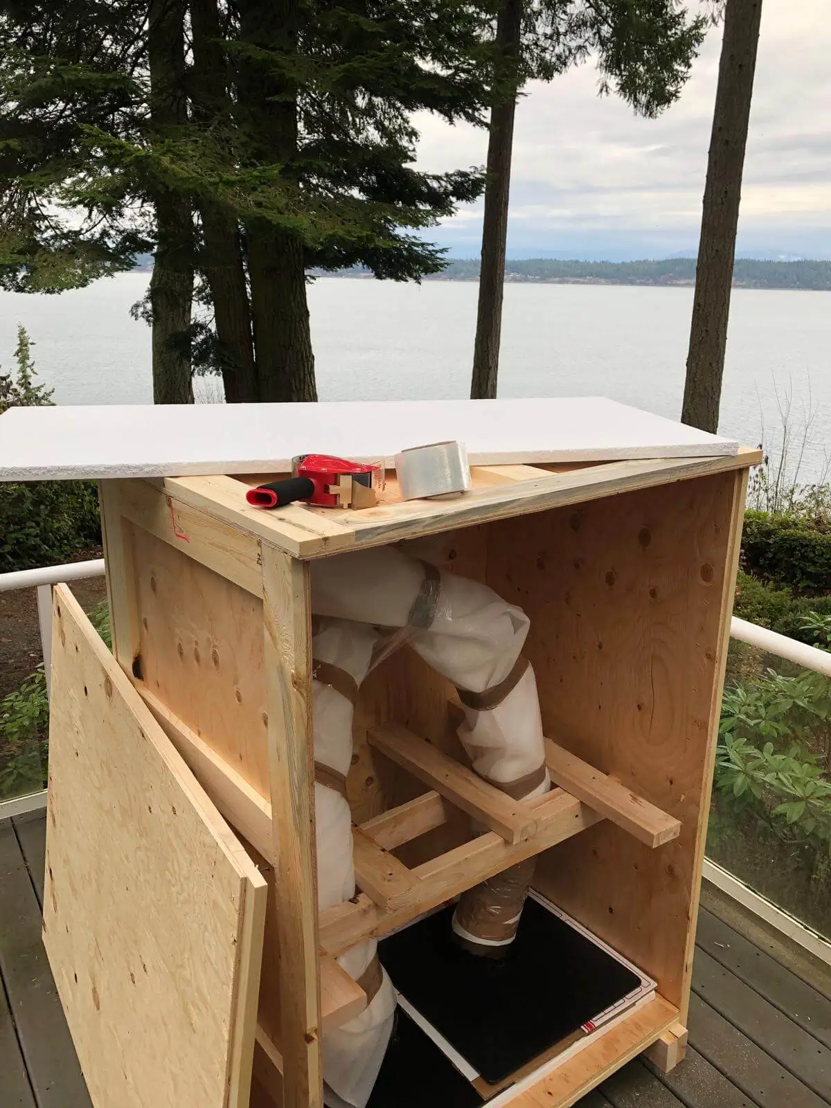 An open crate on a deck with a wrapped piece bedded inside, water beyond.
