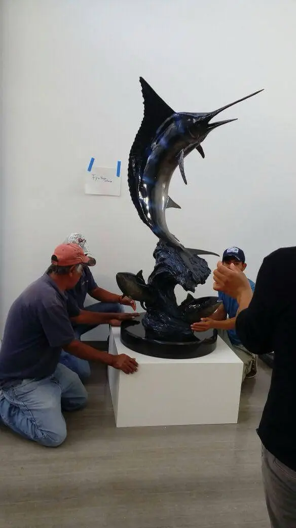 Two crew members steadying a bronze marlin sculpture on its plinth before crating.