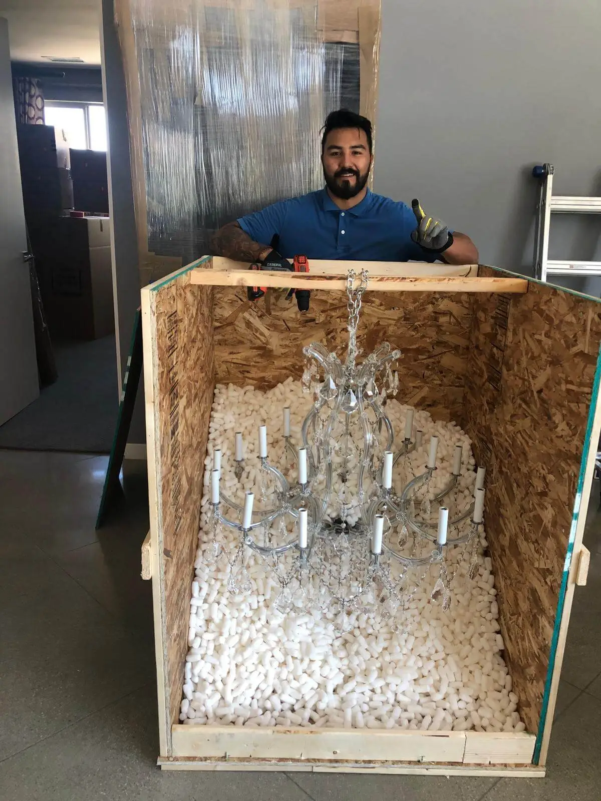 A crystal chandelier packed in loose fill, a crew member steadying the crate.