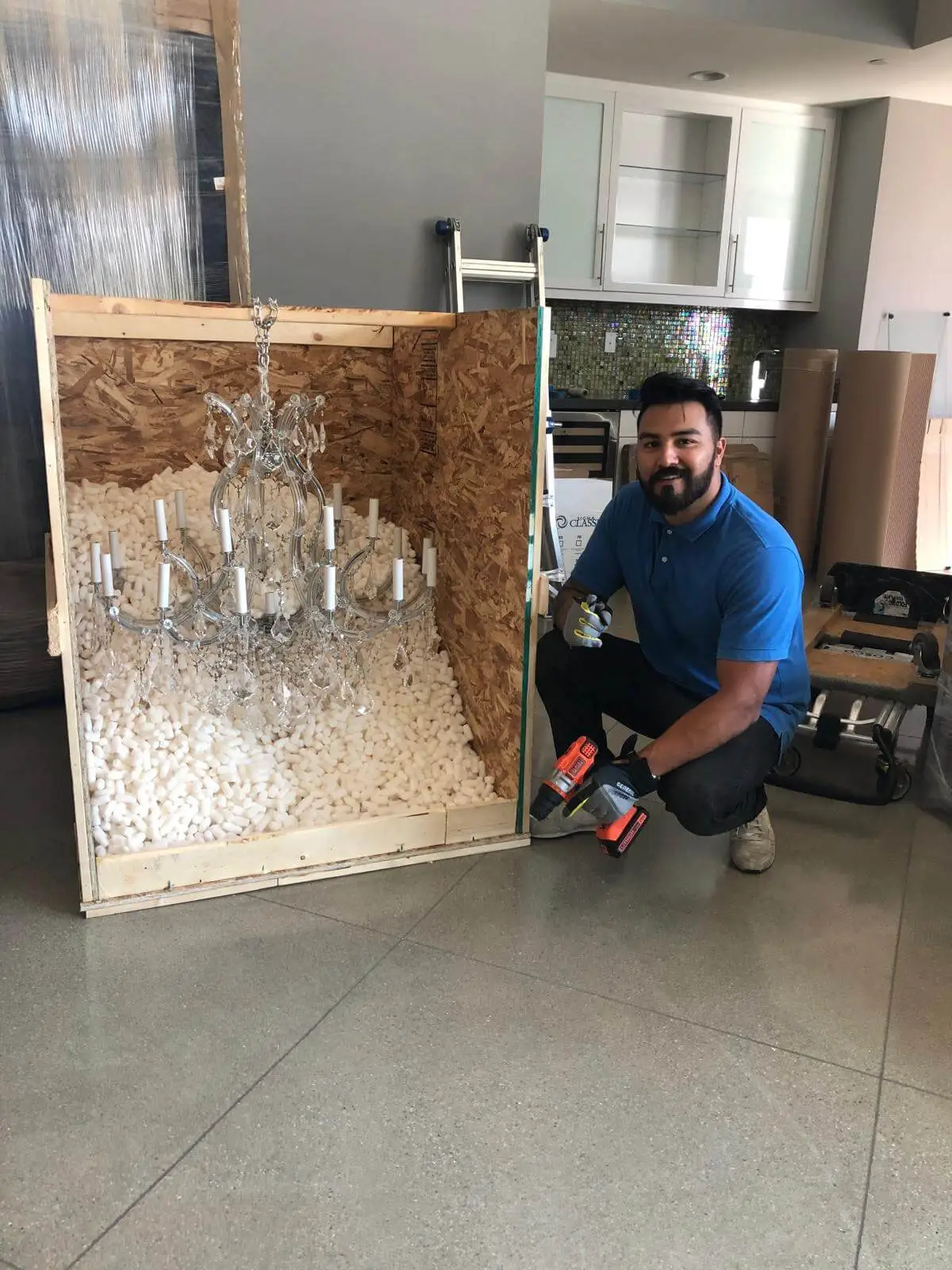 A chandelier bedded into loose fill inside a purpose-built crate, a crew member checking the packing.