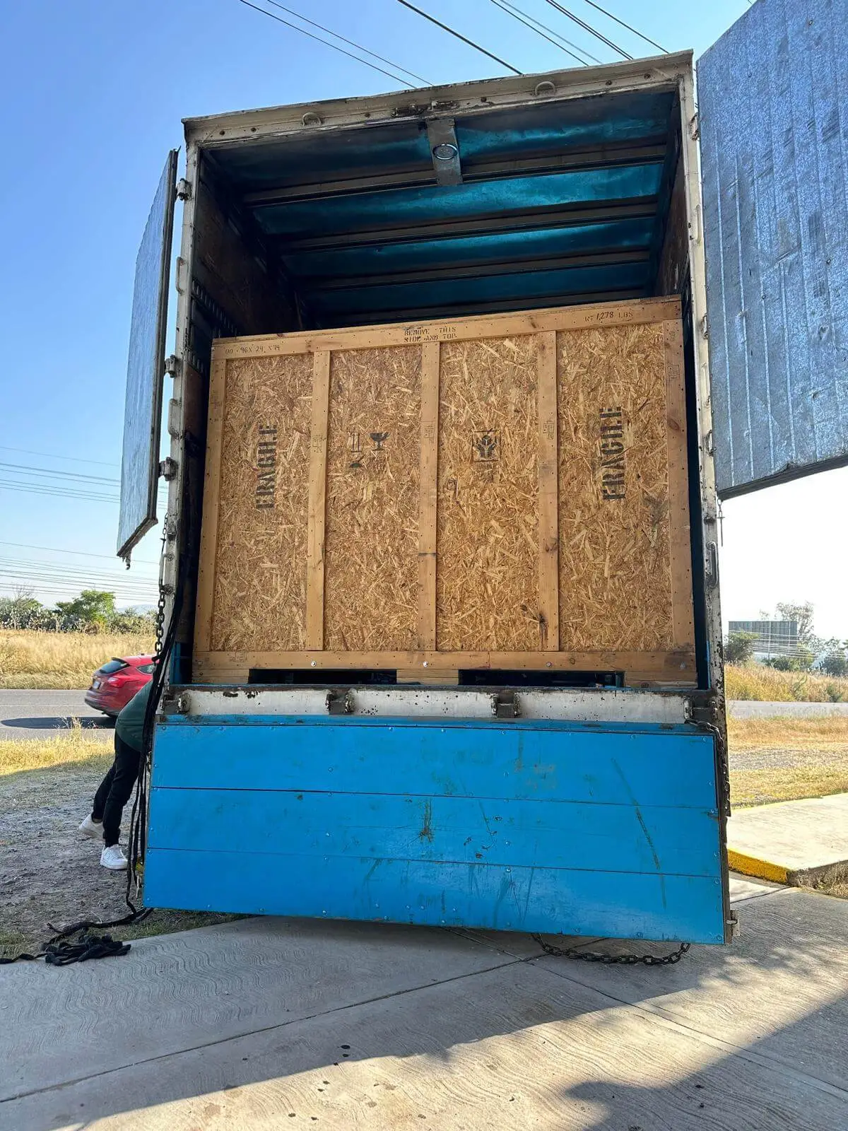A large plywood crate riding the truck's lift gate during loading.