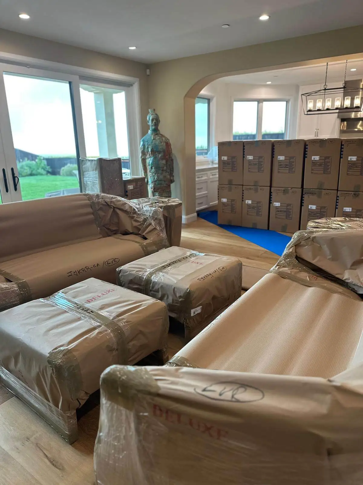 Wrapped seating and labelled cartons staged on floor protection, lake view beyond.