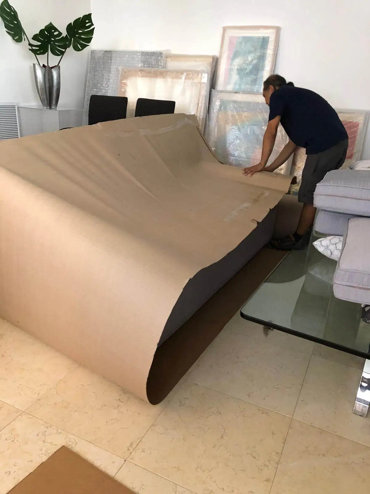A crew member rolling kraft paper over a dining table, framed art stacked behind.