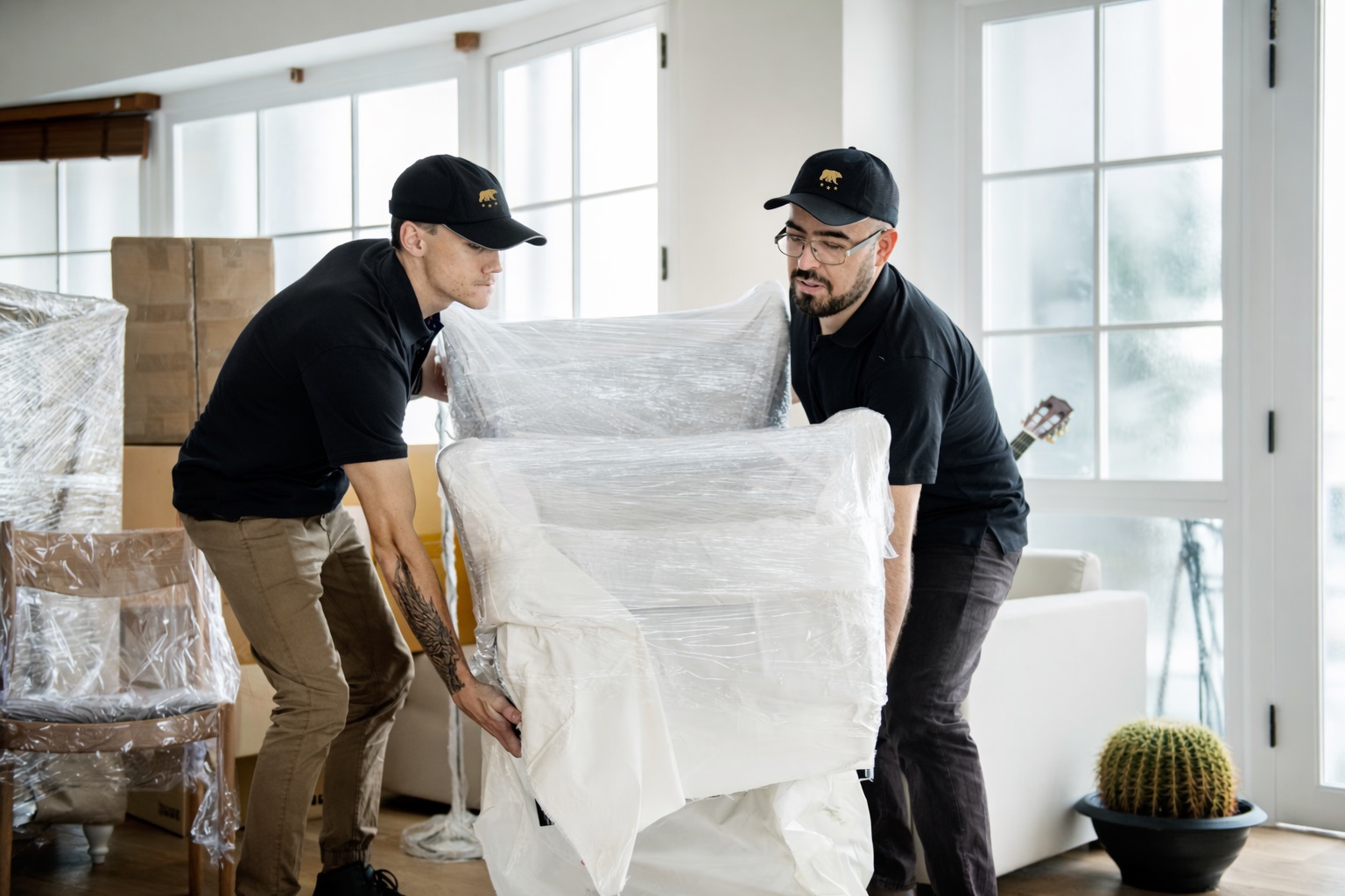 Two Golden Bear crew members wrapping a sofa in protective padding inside a client's home.