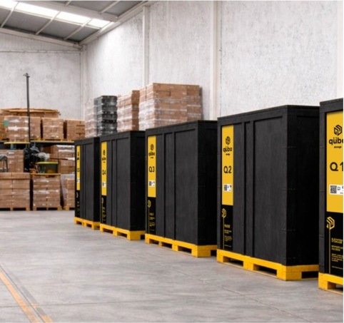 Black Qubo storage crates on yellow pallets lined up in a warehouse.
